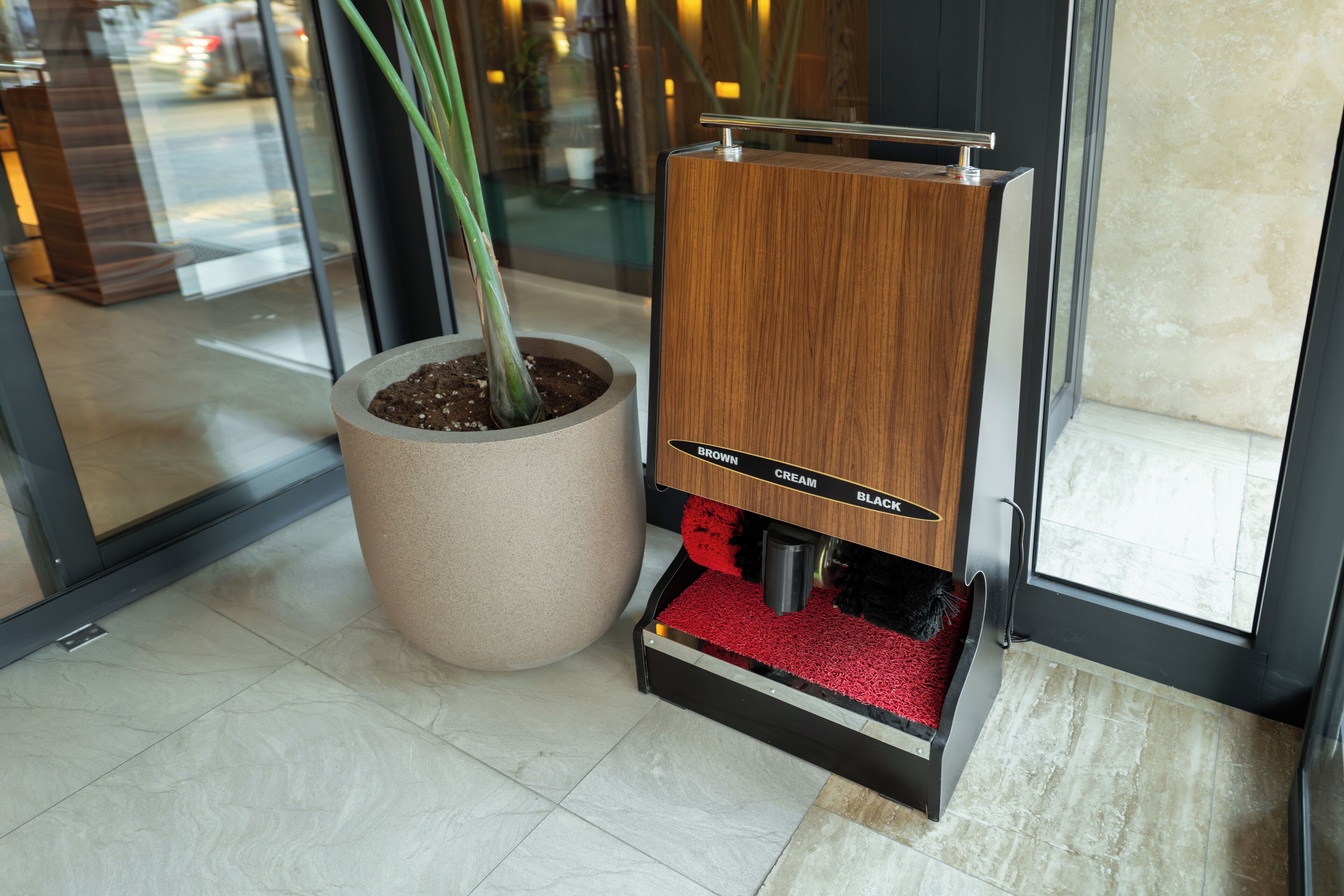 Une machine à café avec un panneau en bois et un bac rouge, placée à côté d’une plante en pot.