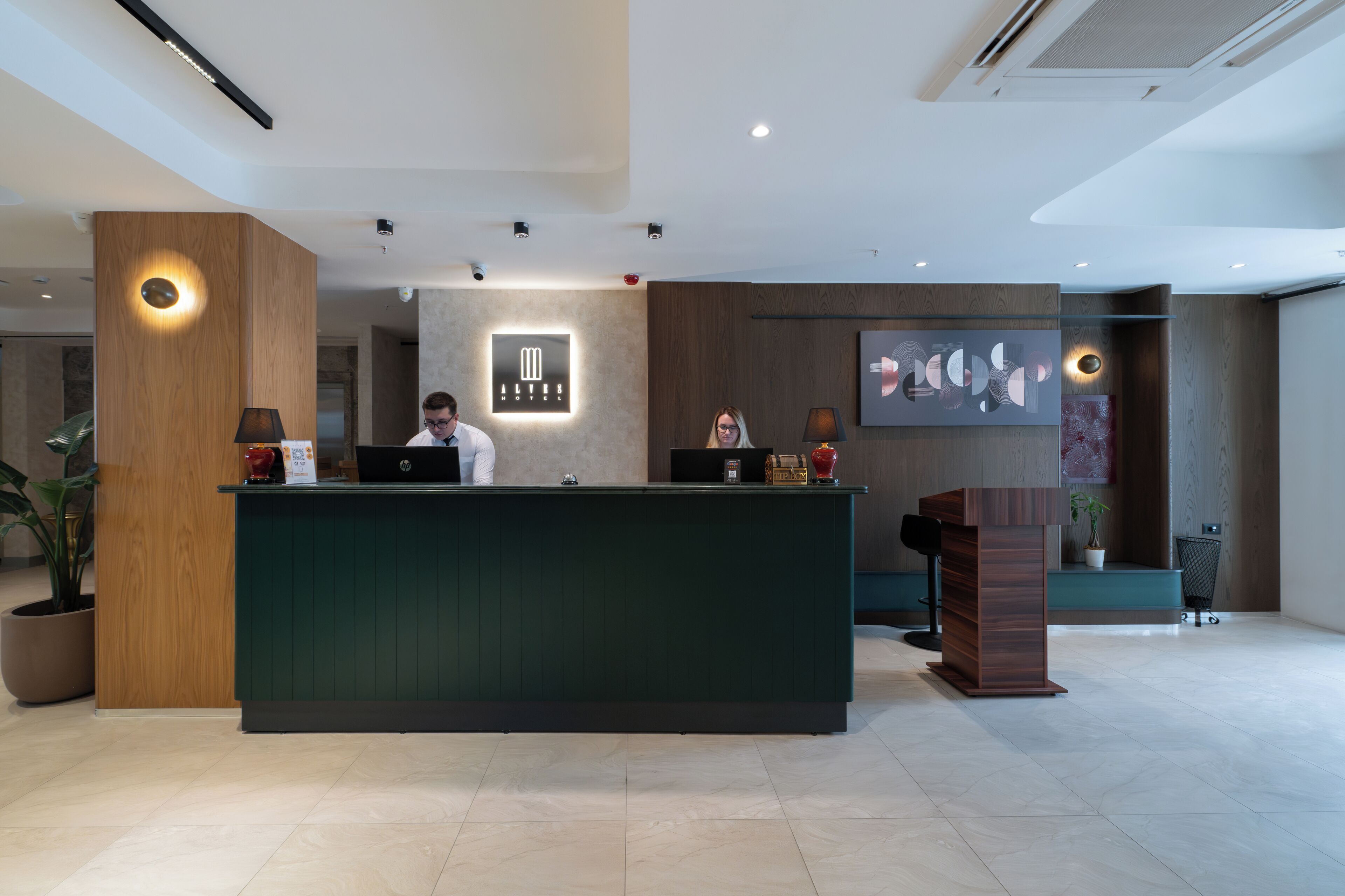 A modern reception desk with a wooden finish, a digital display, and a potted plant.