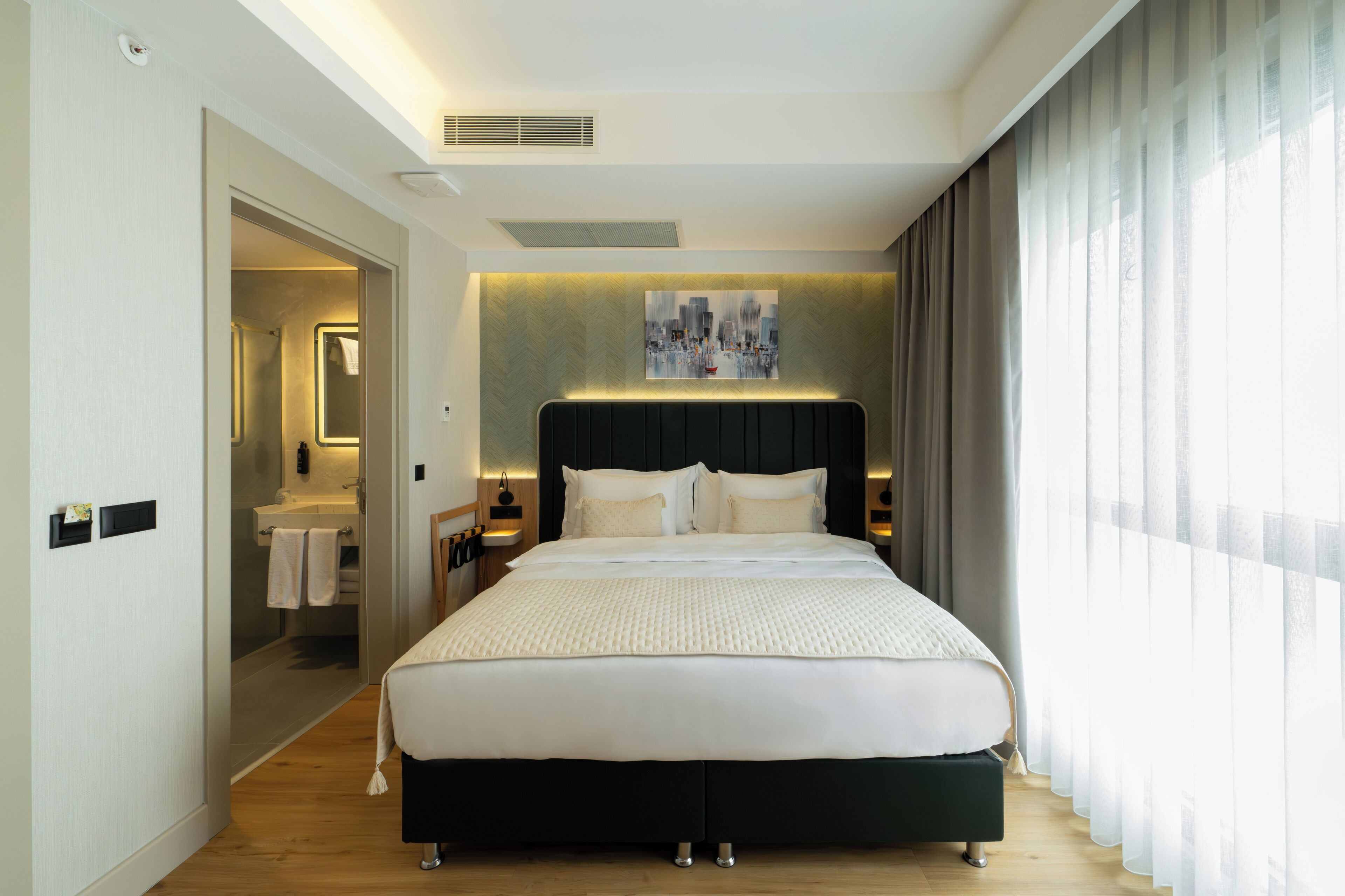 Una habitación de hotel moderna con una cama grande, un baño con ducha y una obra de arte urbana en la pared.