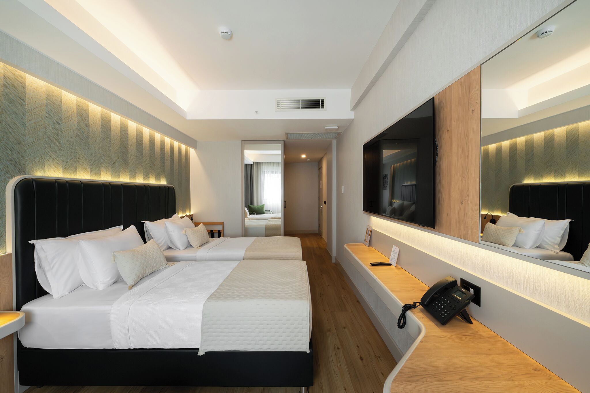 A hotel room with two beds, a bedside telephone, a mirror, and a television.