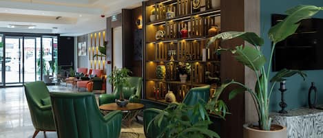 A lobby with green chairs, a coffee table, a large potted plant, and a wall with shelves of decorative items.