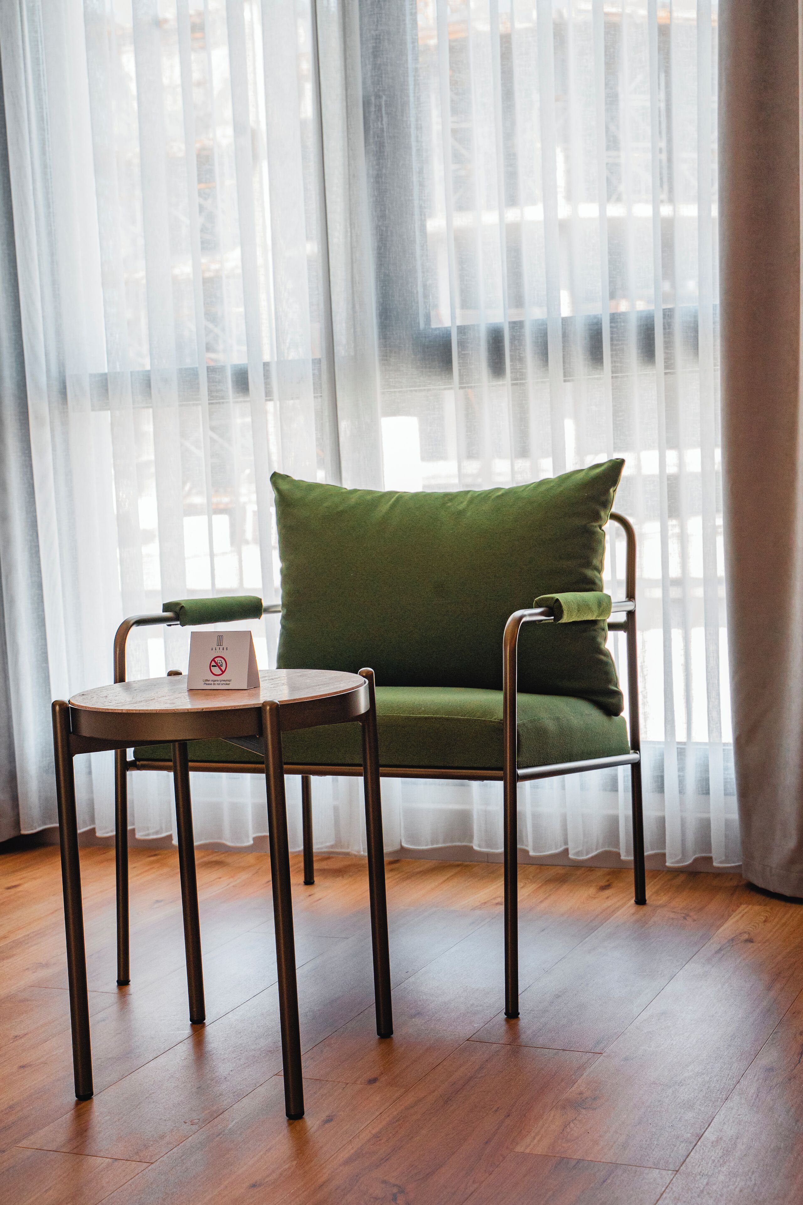 Una habitación con una silla verde acolchada y una pequeña mesa redonda con un letrero.