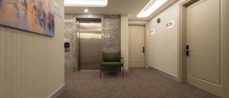 A hotel hallway with a green chair, an elevator, and a door marked "407".