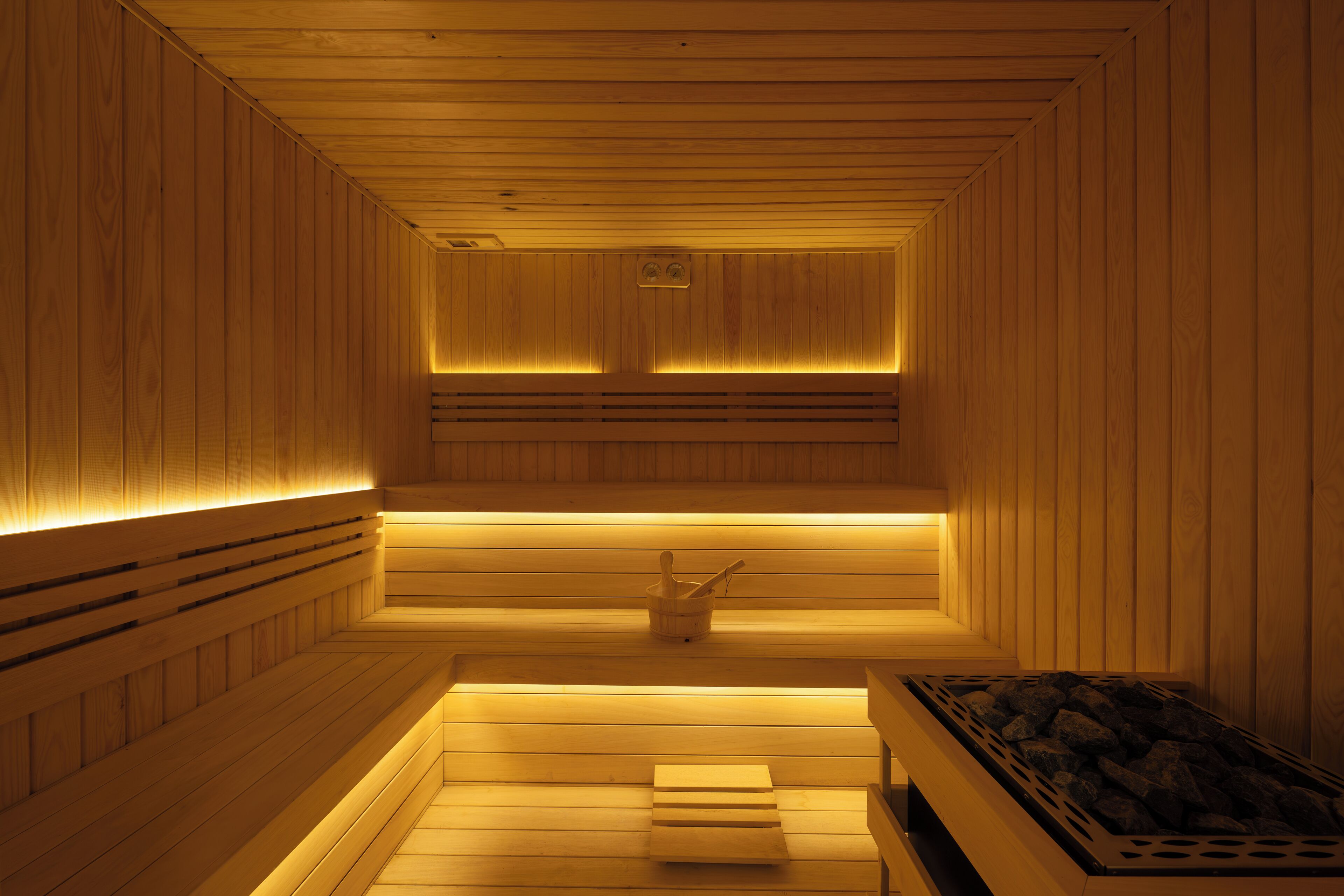 A sauna with wooden walls and benches, a bench with a towel, and a heater with rocks.