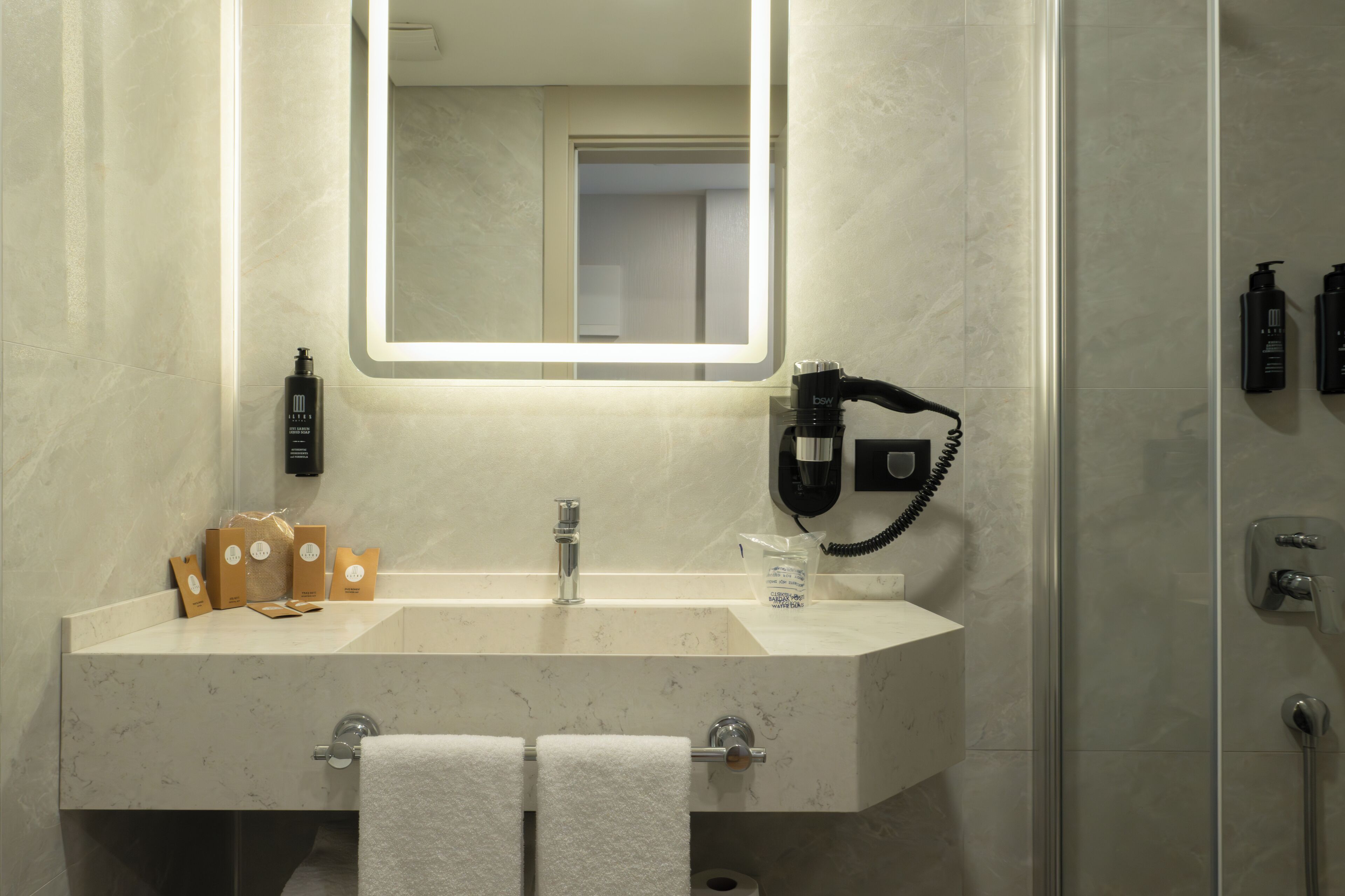 Une salle de bain équipée d’un lavabo en marbre, d’un miroir, d’un sèche-cheveux et d’articles de toilette.