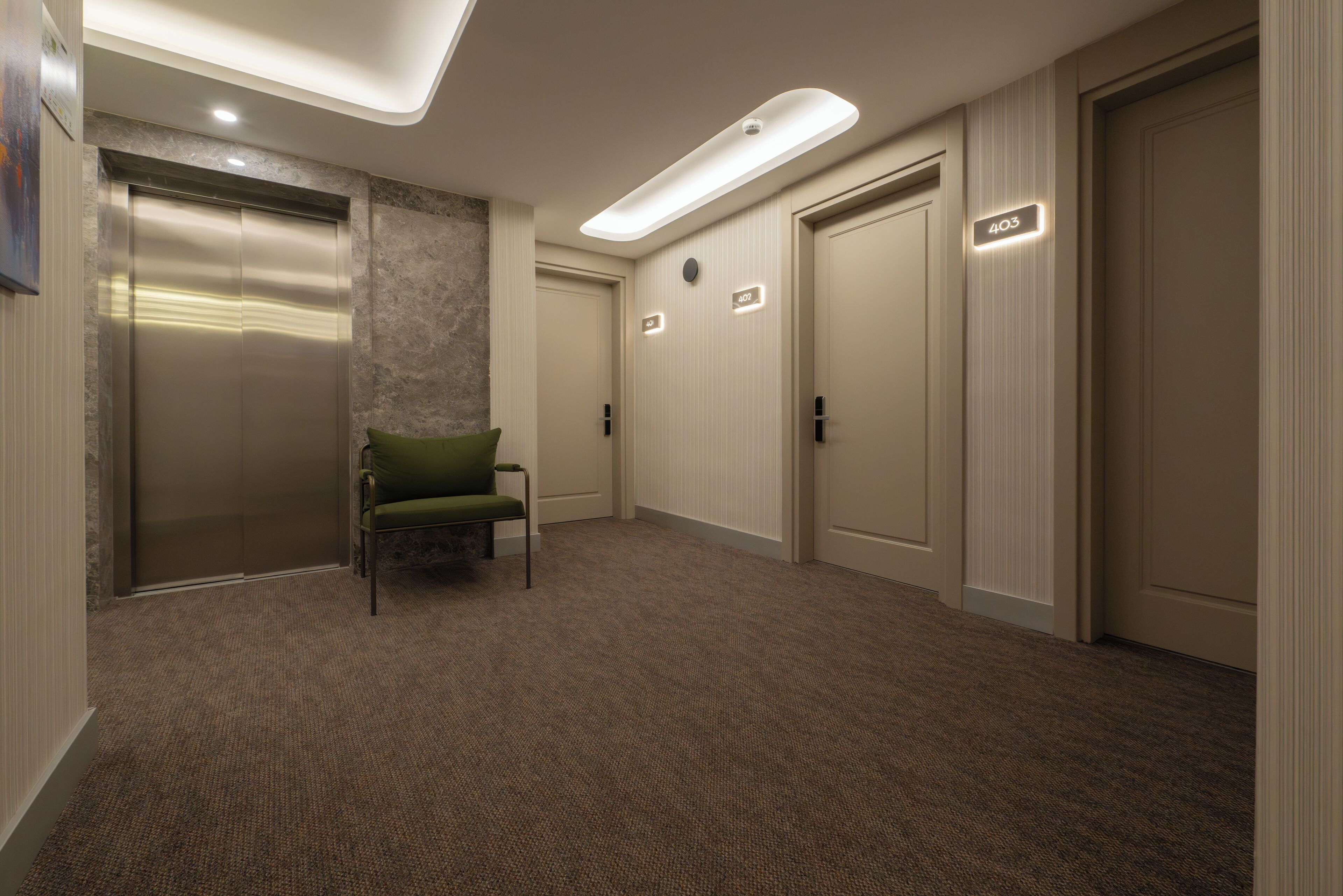 A hotel lobby with an elevator, a green chair, and a carpeted floor.
