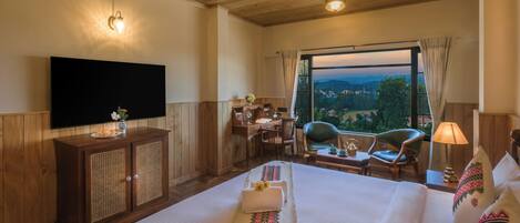 A hotel room with a large bed, a desk, a chair, a television, and a window with a view of the countryside.