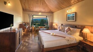A bedroom with a wooden ceiling, a large bed with white linens, a television, a desk with a chair, and a view of the outdoors.