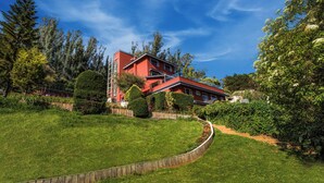 A red building with a sloped roof, surrounded by lush greenery and trees.