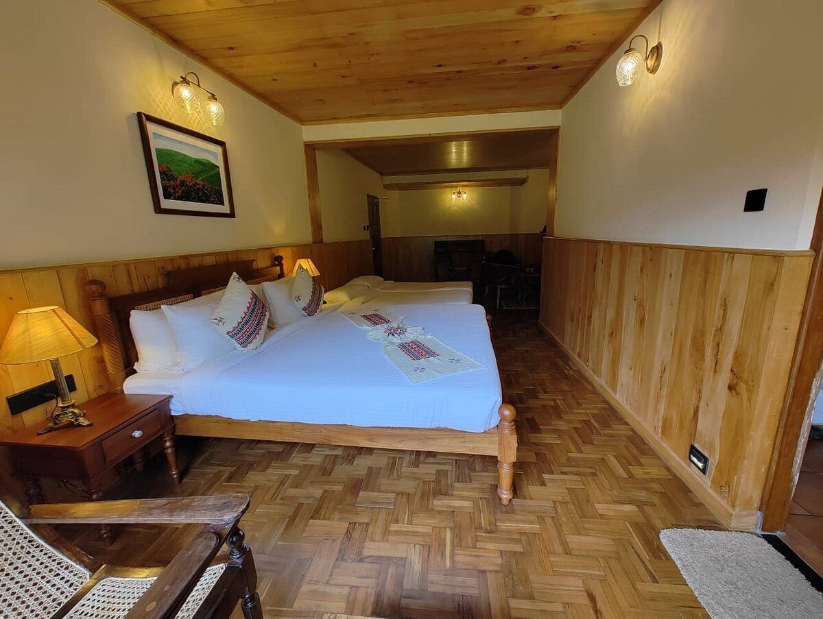 A wooden-paneled room with a large bed, a nightstand, and a chair. There is a framed picture on the wall and a light fixture above the bed.