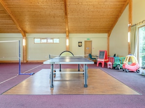 Una mesa de ping pong en una habitación con vigas de madera, un dardo y juguetes infantiles.