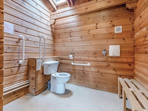 Baño de cabaña de madera con inodoro, barras de apoyo y un banco.