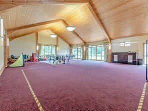 Un espacio interior amplio con techo de madera alto, piso alfombrado color púrpura y varios equipos deportivos.