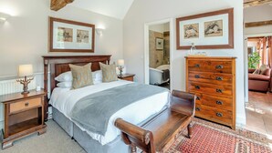 Une chambre à coucher avec un grand lit, une tête de lit en bois, des tables de chevet, une commode et des œuvres d’art accrochées aux murs.