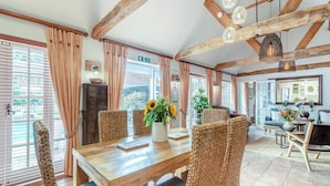 Un vaste espace dédié à la salle à manger, avec une table en bois, des chaises en osier et une vue sur l’extérieur grâce à de grandes fenêtres.