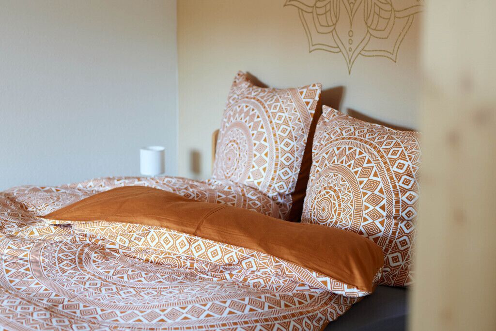 A bed with patterned bedding and a brown pillow.