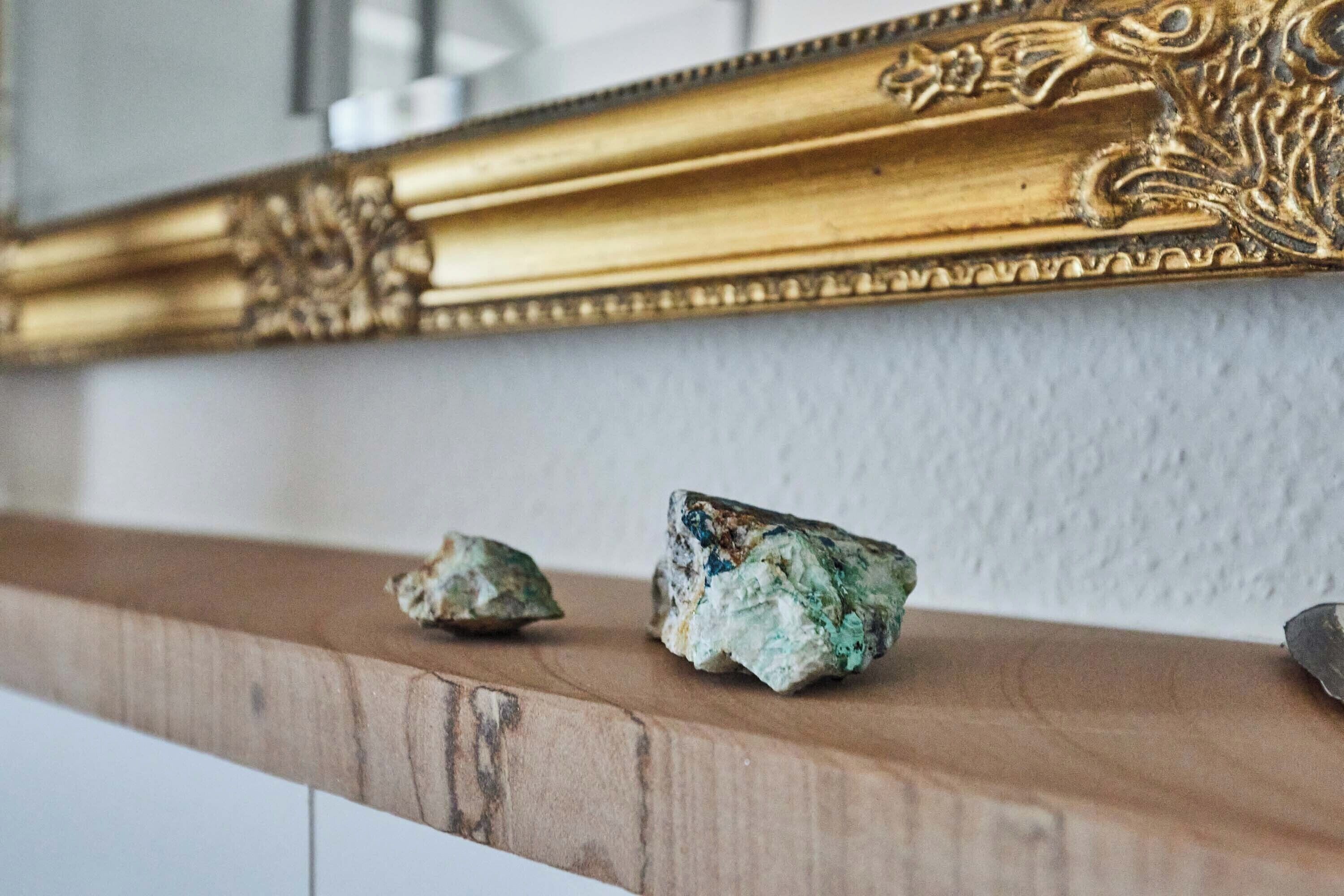 Ein hölzernes Regal mit zwei Steinen und einem goldfarbenen Spiegel.