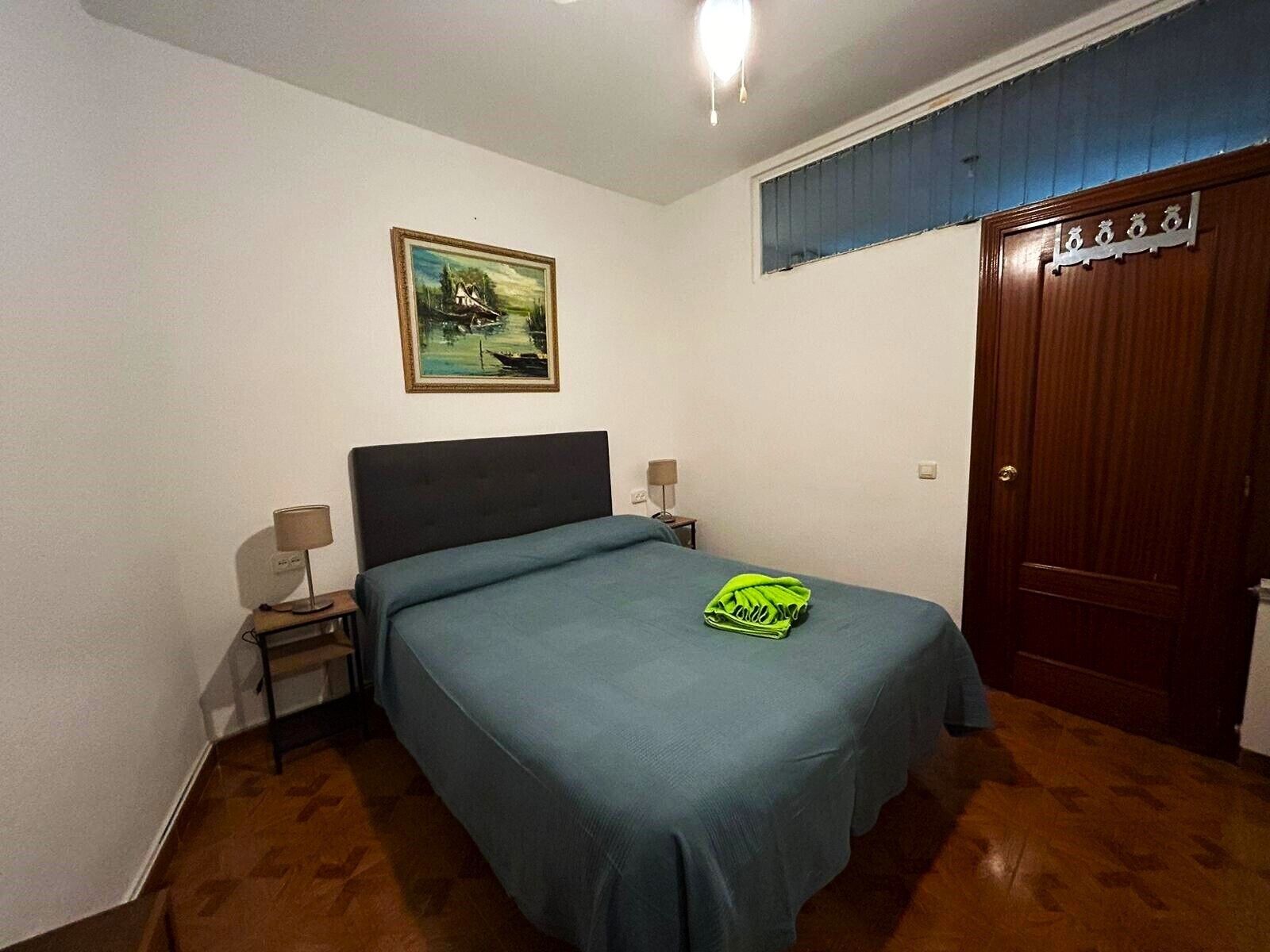 Un dormitorio con una cama individual, una mesita de noche, una lámpara, un cuadro en la pared y una puerta de madera.
