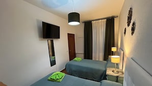 A hotel room with two beds, a TV, a mirror, a ceiling fan, a lamp, and curtains.