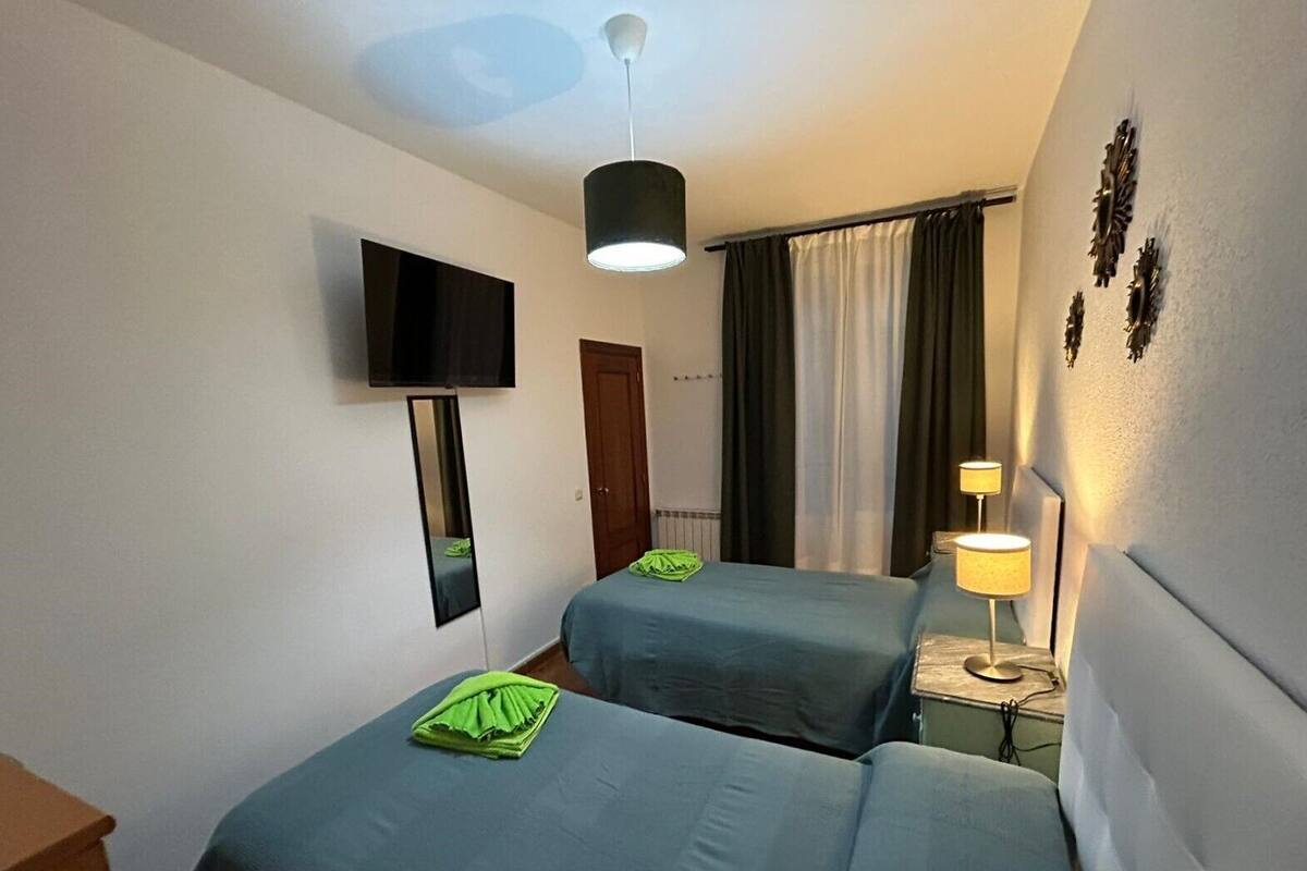 Een hotelkamer met twee bedden, een televisie, een spiegel, een plafondventilator, een lamp en gordijnen.