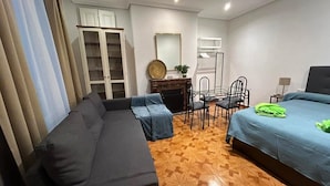 A bedroom with a sofa, a bed, a dining table with chairs, and a wardrobe.