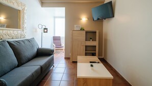 Un salon moderne avec un canapé gris, une table basse en bois, un téléviseur fixé au mur et un petit meuble orné d’une plante.