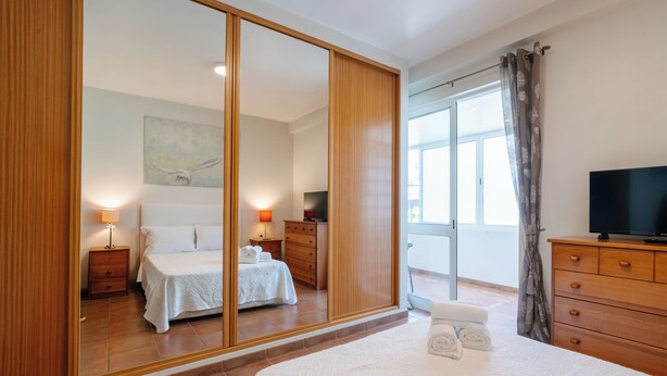Une chambre à coucher avec un grand miroir, un lit, une commode, un téléviseur et une fenêtre avec des rideaux.