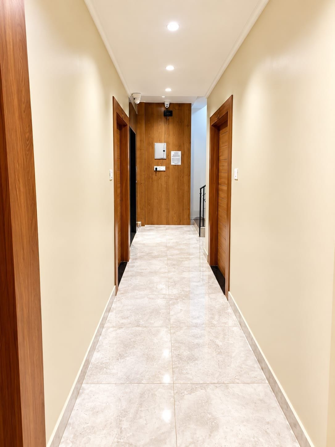 A hallway with wooden doors, a tiled floor, and a ceiling with recessed lighting.