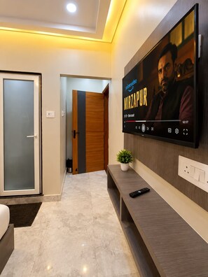 Un salon moderne avec un téléviseur à écran plat fixé au mur, diffusant un film intitulé « MIRZAPUR ».