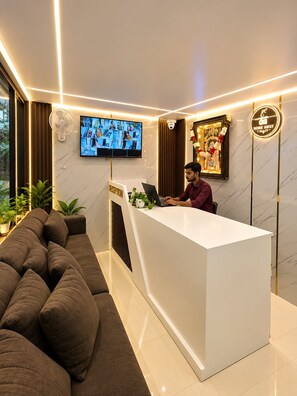 Un área de recepción con un sofá, mostrador de recepción, televisor y una decoración de pared.