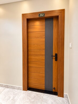 Puerta moderna con placa de número, panel vertical y manija negra.