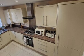 A kitchen with beige cabinets, a gas stove, a microwave, and a toaster. - Spacious 3-bed House - Sleeps 8, Garden & Parking (Peterborough)
