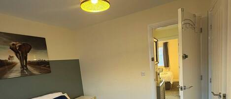 Une chambre d’hôtel avec un lit, un tableau, un luminaire au plafond et une porte donnant sur une autre pièce.