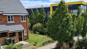 A residential area with a two-story house, a small garden, and a modern building with large windows. - Spacious 3-bed House - Sleeps 8, Garden & Parking (Peterborough)