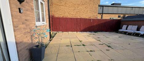 A patio area with a brick wall, a red fence, and a row of white chairs.