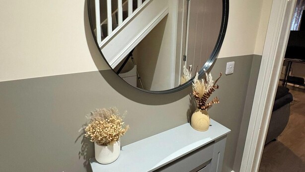 A hallway with a round mirror on a white console, a staircase, and a door. - Spacious 3-bed House - Sleeps 8, Garden & Parking (Peterborough)