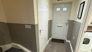 A hallway with a carpeted staircase, a door with an exit sign, and a washing machine in the background. - Spacious 3-bed House - Sleeps 8, Garden & Parking (Peterborough)