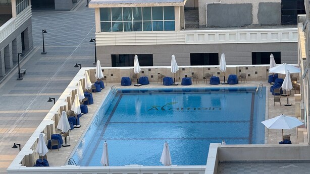 Une piscine sur le toit, avec une eau bleue, entourée de chaises longues et de parasols, et un bâtiment en arrière-plan.