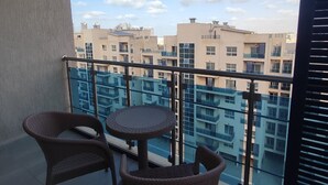 Un balcon avec deux fauteuils en osier et une petite table ronde, donnant sur un quartier résidentiel composé de plusieurs immeubles.