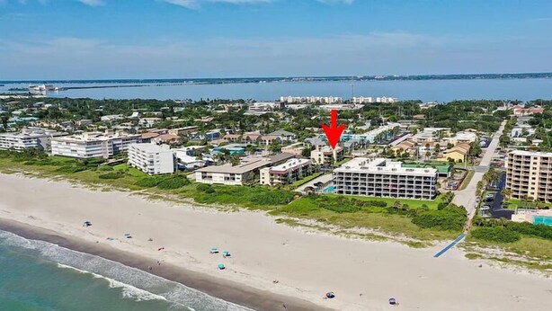 Vista aérea de una zona costera con una playa, edificios de hotel y una masa de agua al fondo.