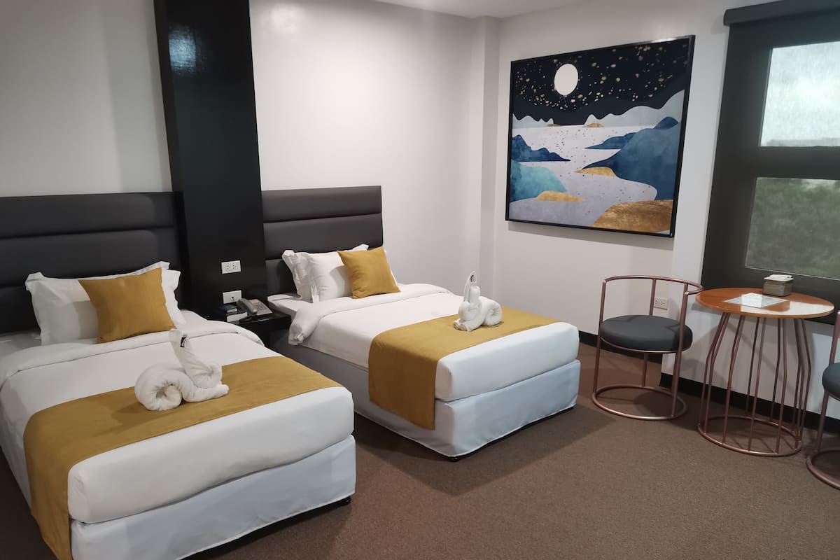Habitació d'hotel amb dos llits, una tauleta de nit, una taula petita i un quadre al mur.