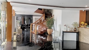A modern hotel lobby with a marble floor, a wooden staircase, a reception desk, and a large potted plant. - Palette in Angeles, Pampanga near Clark International Airport (Formerly Boss Hotel) (Angeles City)