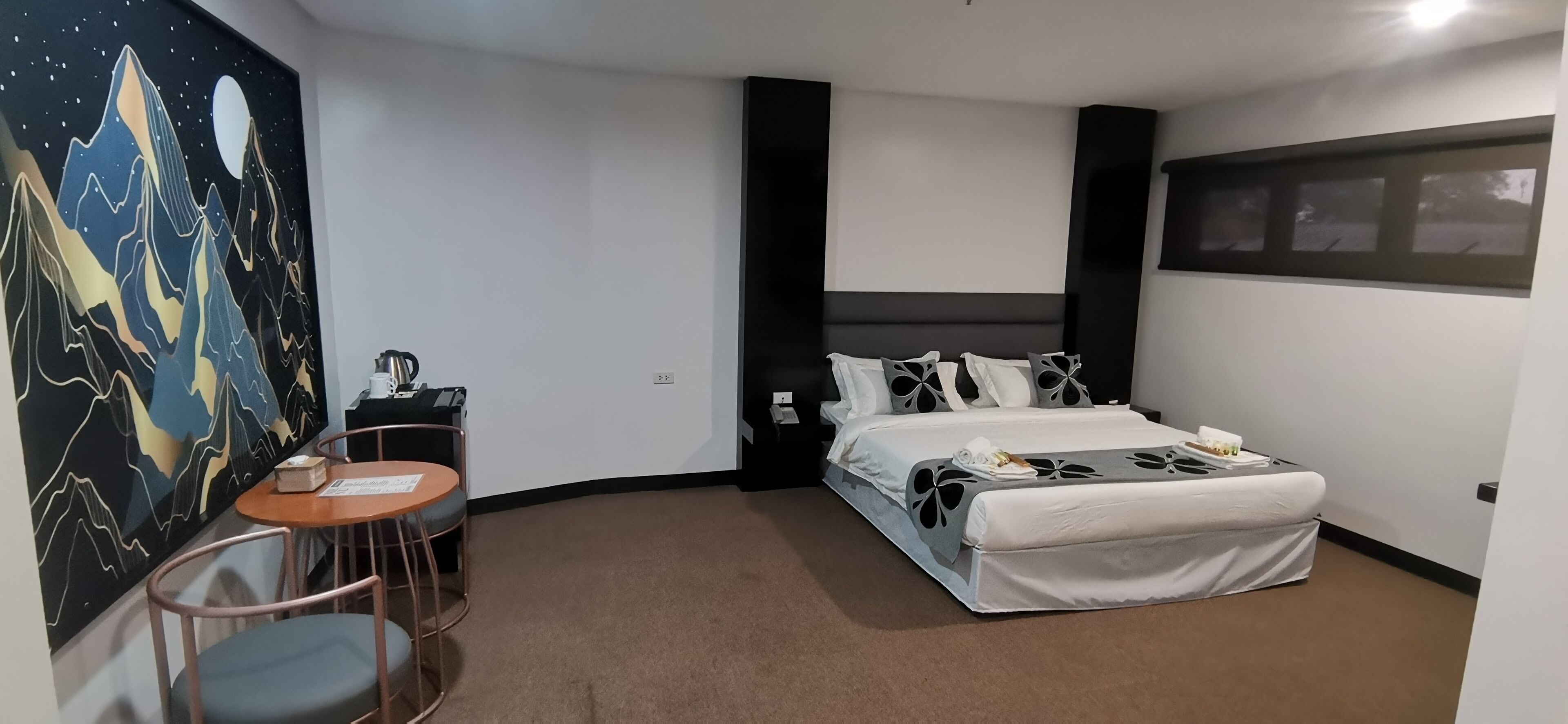 A hotel room with a bed, a desk, a chair, and a wall painting.