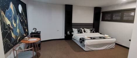 A hotel room with a bed, a desk, a chair, and a wall painting.