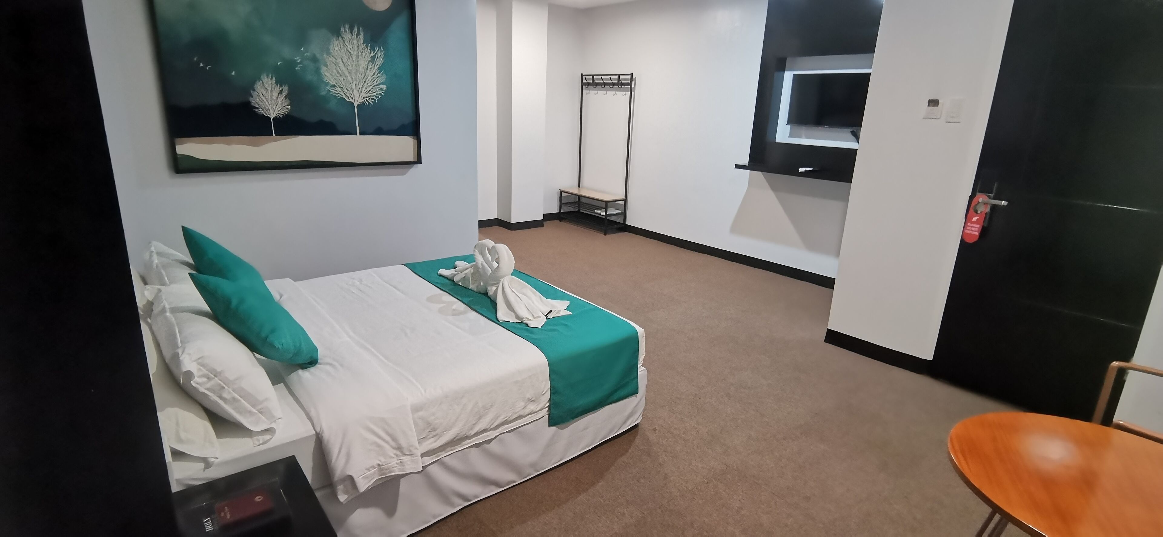 A hotel room with a bed, a chair, a coat rack, and a painting on the wall.