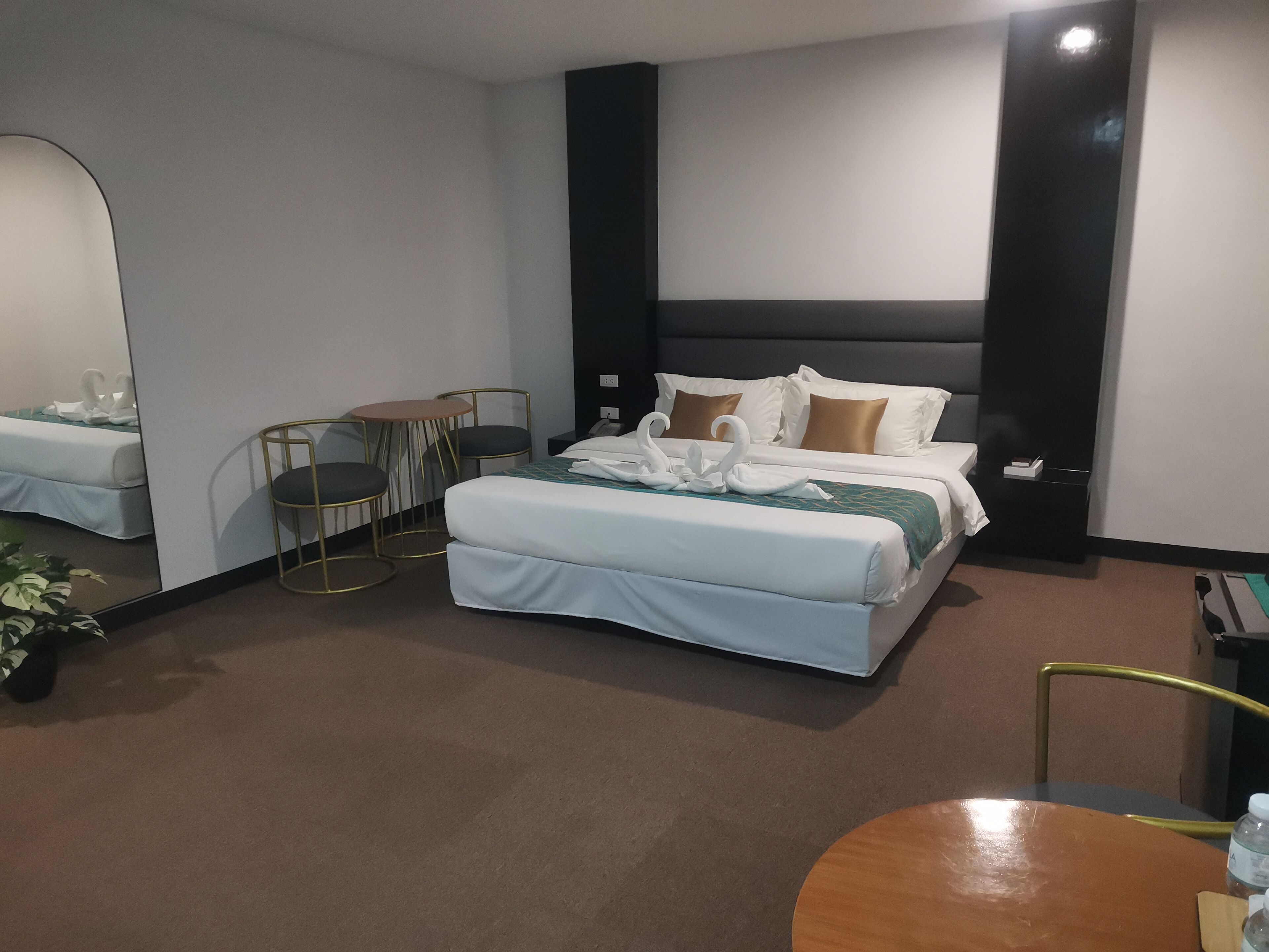 A hotel room with a large bed, a small round table with two chairs, a mirror, and a nightstand.