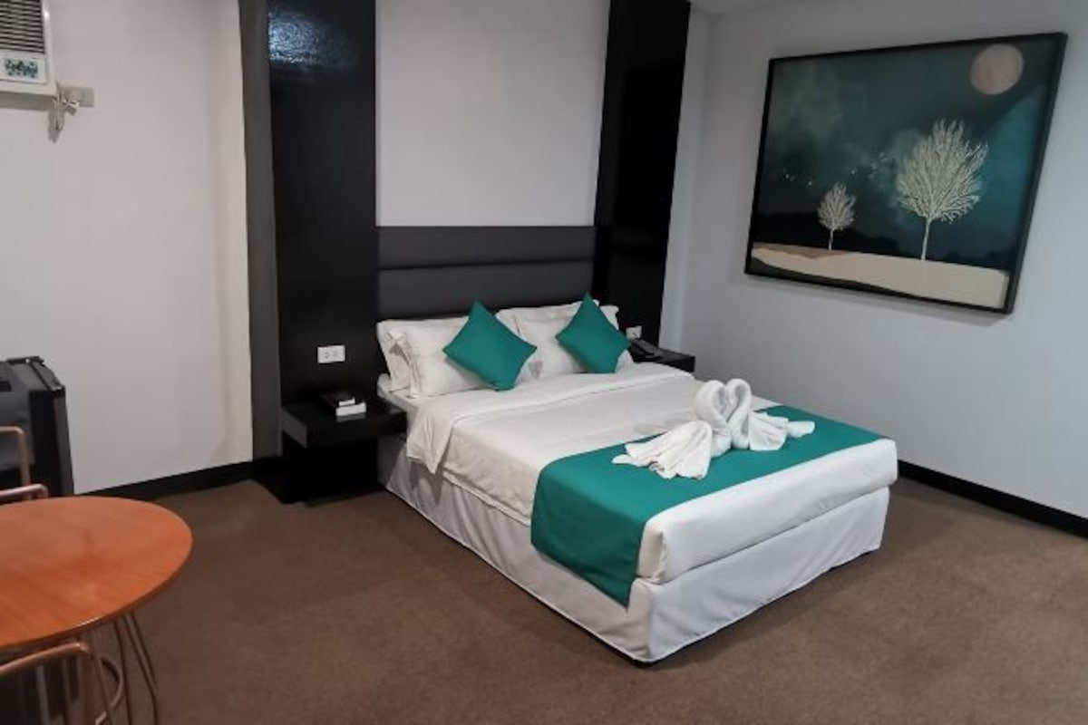 A hotel room with a bed, nightstands, a table, and a painting on the wall.