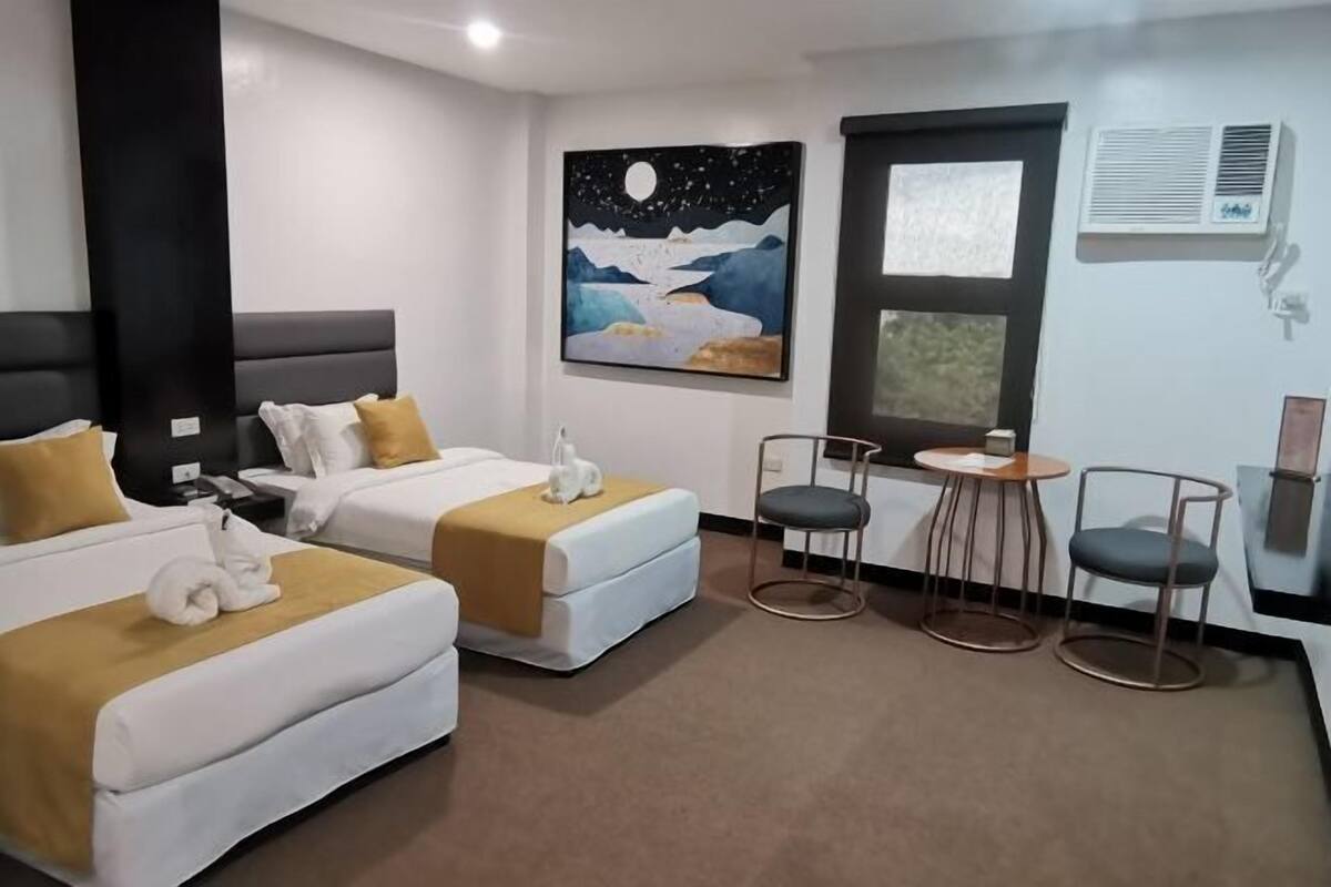 Habitació d'hotel amb dos llits, una pintura del cel nocturn, una finestra i una taula petita amb cadires.