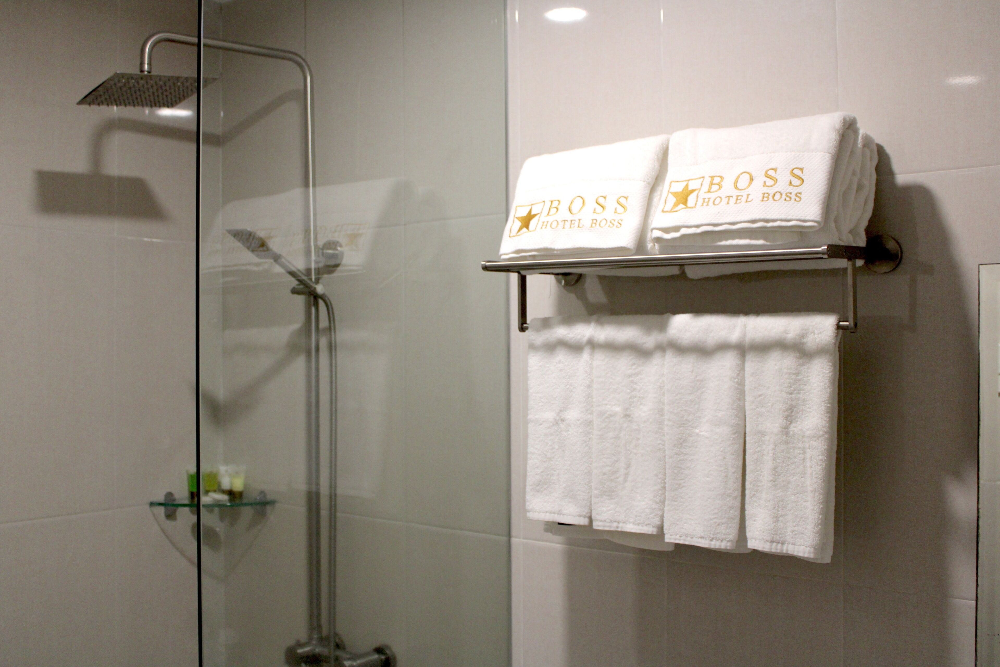A bathroom with a glass-enclosed shower, a towel rack with two towels, and a small shelf with toiletries.