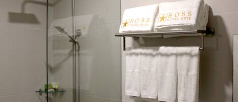 A bathroom with a glass-enclosed shower, a towel rack with two towels, and a small shelf with toiletries.